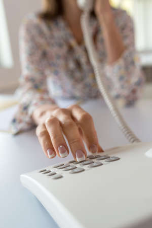 Closeup of a business assistant with perfect french manicure dialing a telephone number using a...
