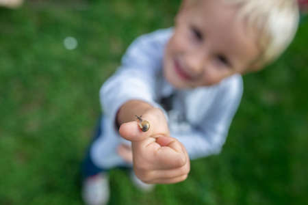 Top view of cute toddler child standing on green grass showing a tiny snail on his finger to the camera.の写真素材