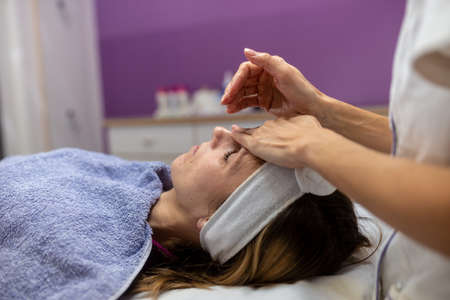 Young woman lying on massage table getting a facial treatment and moisturizing massage in a cosmetic...