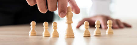 Wide view image of business leader placing king chess figure on the leading position in front of...