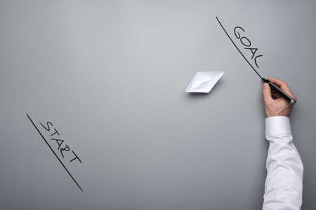 Conceptual image of business vision - origami paper boat floating towards a goal line over grey background.の写真素材