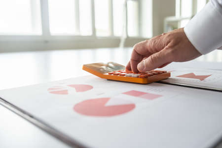 Closeup of financial advisor using calculator as he reviews statistical graphs and charts.の写真素材