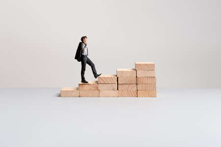 Businessman climbing up the steps made of wooden pegs in a conceptual image of business vision and determination.の写真素材