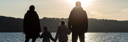 Wide view image of silhouette of a family with two kids holding hands by the sea looking in to the distance.の写真素材