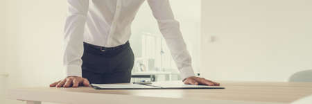Wide view image of businessman leaning on his office desk with paperwork in a folder and ink pen in front of him.の写真素材