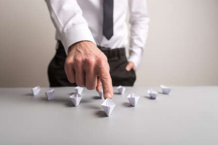Businessman pushing forward the leading paper made boat in an arrow shape in a conceptual image of business leadership.の写真素材