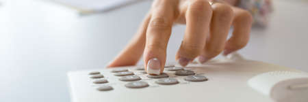Wide view image of a woman with perfect french manicure dialing a telephone number using white landline phone.の写真素材