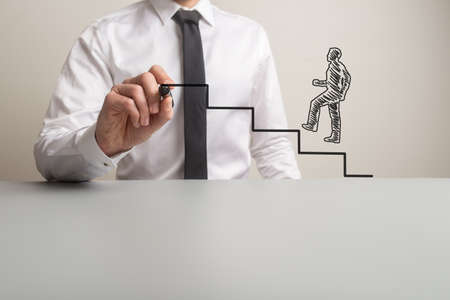Business executive drawing steps for a handdrawn businessman to climb in a conceptual image. With copy space.の写真素材