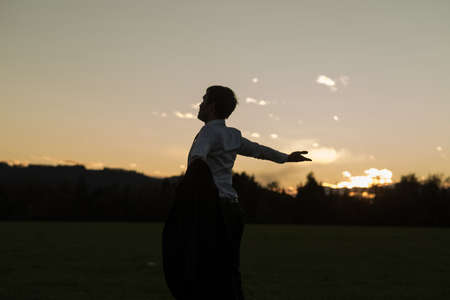 Young businessman enjoying his freedom holding his suit jacket standing in meadow under evening sky.の写真素材