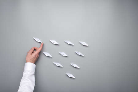 Hand of a businessman pushing one of the origami paper made boats forward to stand out from the group.の写真素材
