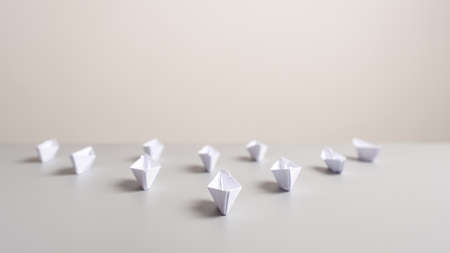 Paper made origami boats placed on an office desk in an arrow shaped position in a conceptual image.の写真素材