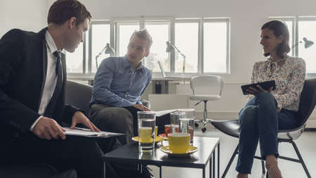 Three business people sitting around a coffee table in an office having a meeting.