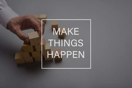 Make things happen sign in front of a male hand assembling a pyramid of wooden blocks.の写真素材