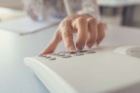 Closeup view of female receptionist dialing a telephone number using white landline phone.の写真素材