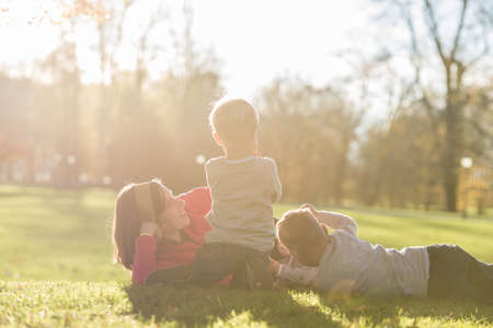 Mother lying in a grass in a park with her three kids around her lit by a bright sun in a conceptual...