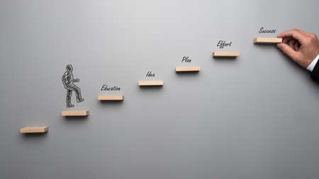 Silhouetted businessman walking up the stairs towards success with words Education, Idea, Plan and Effort along the way. Over grey background.の写真素材