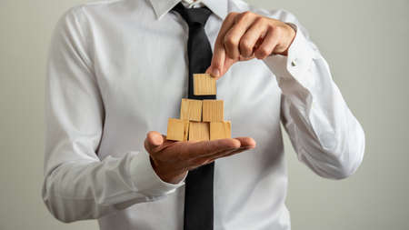 Businessman making a little pyramid of wooden blocks in the palm of his hand.の写真素材
