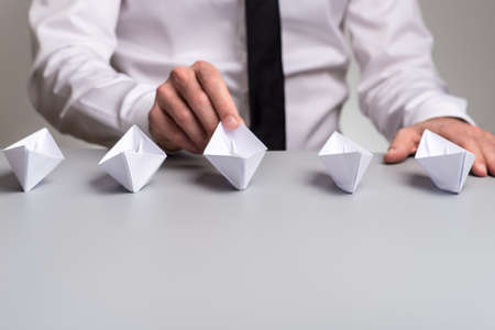 Businessman sitting at his desk with five origami paper boats in front of him.の写真素材