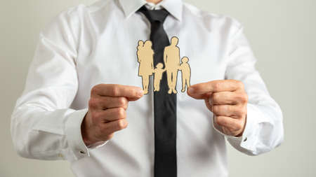 Front view of a man holding paper cut silhouette of a family showing it to the camera. Over grey background.の写真素材