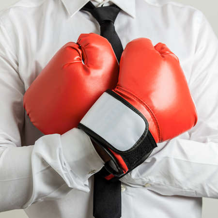 Closeup view of businessman wearing red boxing gloves with his arms crossed on his chest.の写真素材