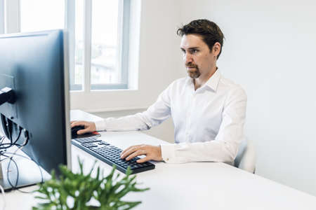 Serious young businessman sitting at his office desk working on his computer.