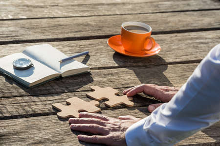 Businessman leaning on his wooden desk brainstorming for new ideas. Puzzle pieces, notebook, compass...