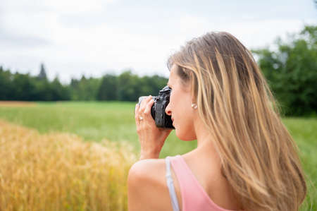 View from behind over the shoulder of a young female photographertaking a photo with black dslr...