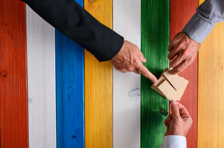 Teamwork concept - top view of three male hands stacking wooden pegs over colourful wooden background.の写真素材