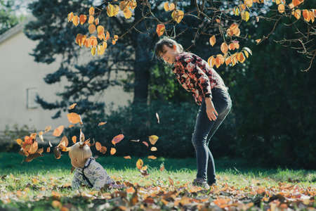 Happy young mother playing and having fun with her little baby son throwing autumn leaves in the air.の写真素材