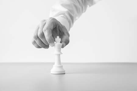 Greyscale image of a businessman placing a king chess figure on adesk in a conceptual image.の写真素材