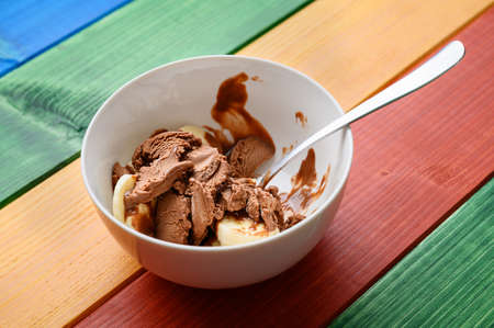 White cup of chocolate ice cream with fresh banana slices on colorfulwooden desk.の写真素材