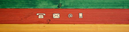 Wide view image of contact and communication icons cut out of paper placed in a row over a...