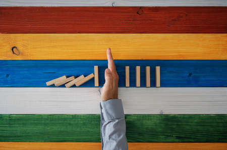 Top view of a hand of businessman stopping dominoes from falling over colorful background of wooden...