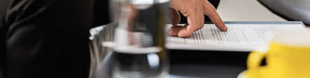 Wide low angle view of businessman proofreading a document or contract while drinking coffee.