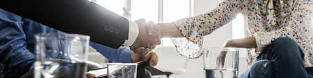 Wide view image of businessman and businesswoman shaking hands in agreement as the sit in a meeting at an office coffee desk.