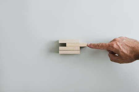 Male hand pushing wooden peg to complete a solid and stable stack of them. Over grey background with...
