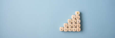 Wooden dices with light bulb symbols placed in a stairway like structure with the light bulb on top glowing yellow.の写真素材