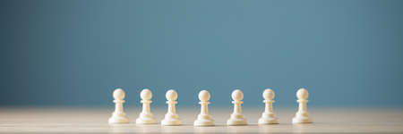 Seven white pawn chess figures placed in a row in a conceptual image.