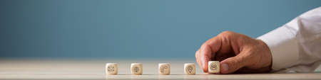 Wide view image of hand of a businessman placing wooden cubes with contact, communication and location icons in a row.の写真素材