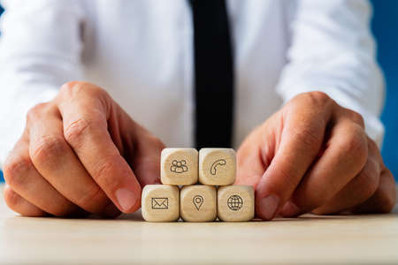 Hands of a businessman holding wooden dices with contact and communication icons of customer service...