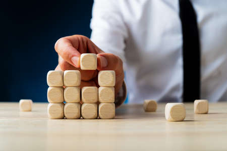 Businessman placing the last dice in a stacked structure in a conceptual image of new business. Over...