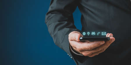 Businessman holding mobile phone with contact and communication icons glowing above it in a...