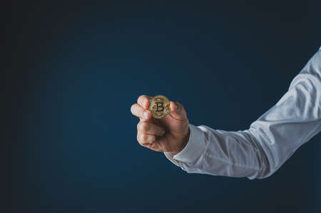 Hand of a businessman holding a golden coin of crypto currency Bitcoin. Over navy blue background.の写真素材