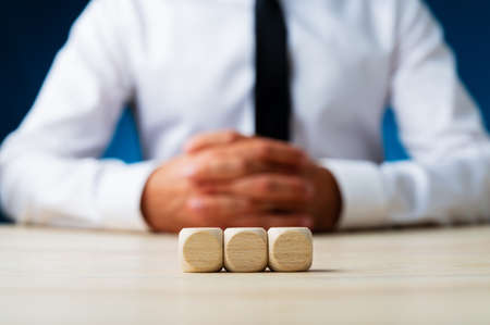 Three blank wooden dices in a row with blurred businessman in background.の写真素材