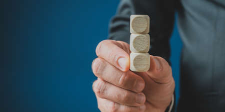 Hand of a businessman holding a stack of three blank wooden dices. Over navy blue background with copy space.の写真素材