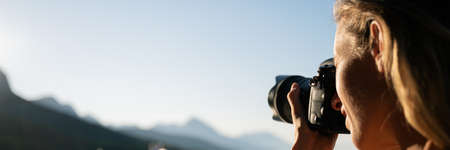 Wide view image of a young female photographer taking photos of mountains in the distance.