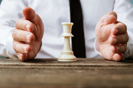 Closeup view of businessman holding protective hands around a white king chess piece.の写真素材