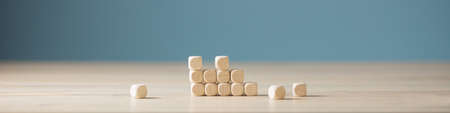Wide view image of an unfinished structure of wooden dices with some of them lying scattered on a desk. Over blue background.の写真素材