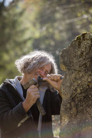 Happy senior sculptor working outside carving in stone using mallet and a chisel.の写真素材