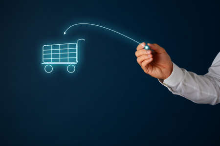 Online shopping concept - male hand drawing an arrow pointing in shopping cart on virtual interface with a gloving pen. Over navy blue background.の写真素材